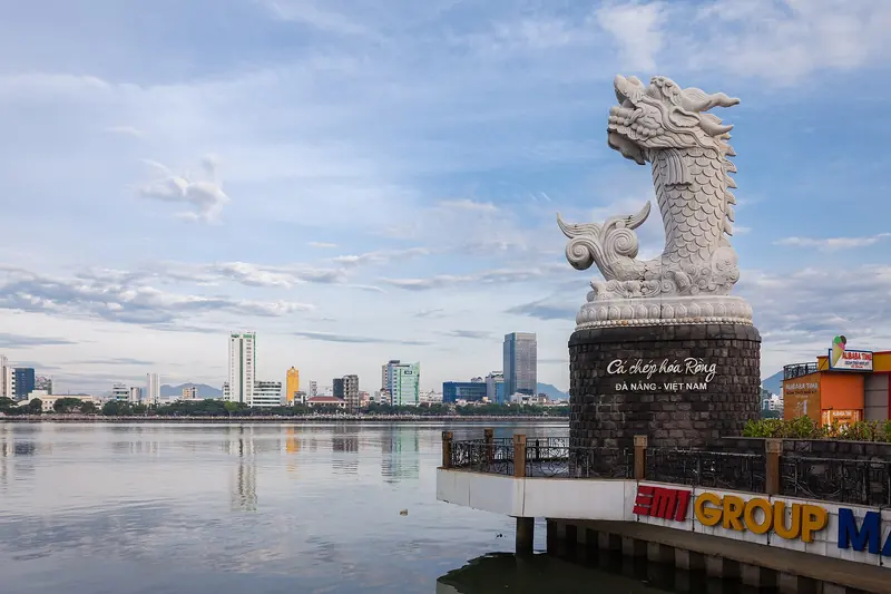 The white carp-dragon statue on the Love Bridge pier, with Da Nang’s riverfront behind